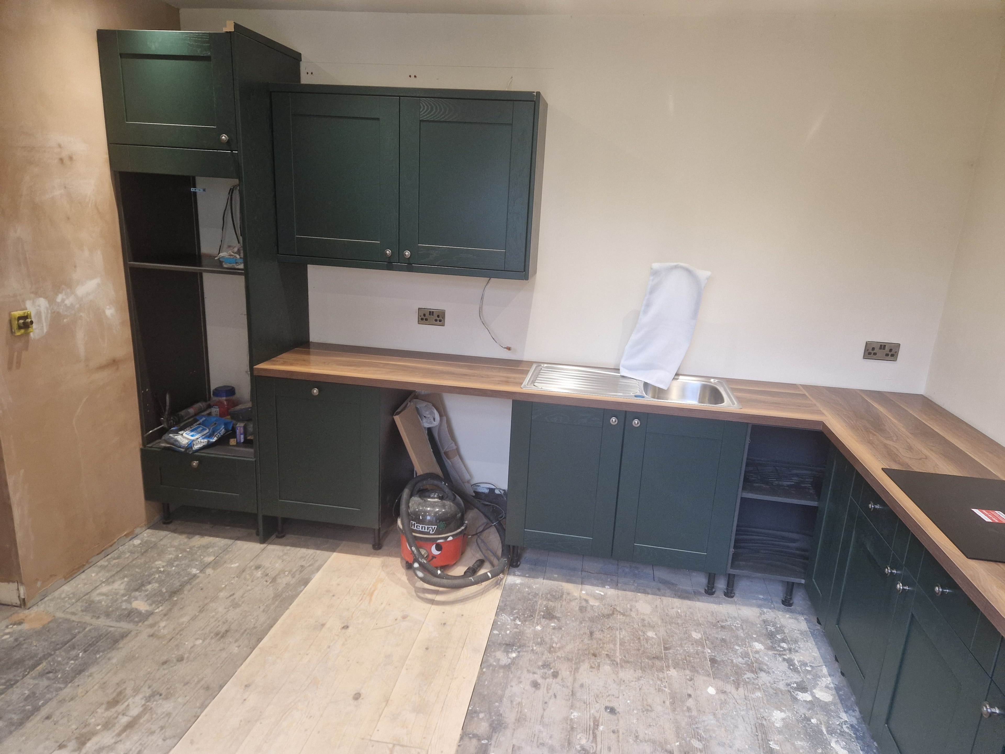 Kitchen installation in progress, with dark green cabinets and timber worktops fitted. The flooring and finishing work are still underway.