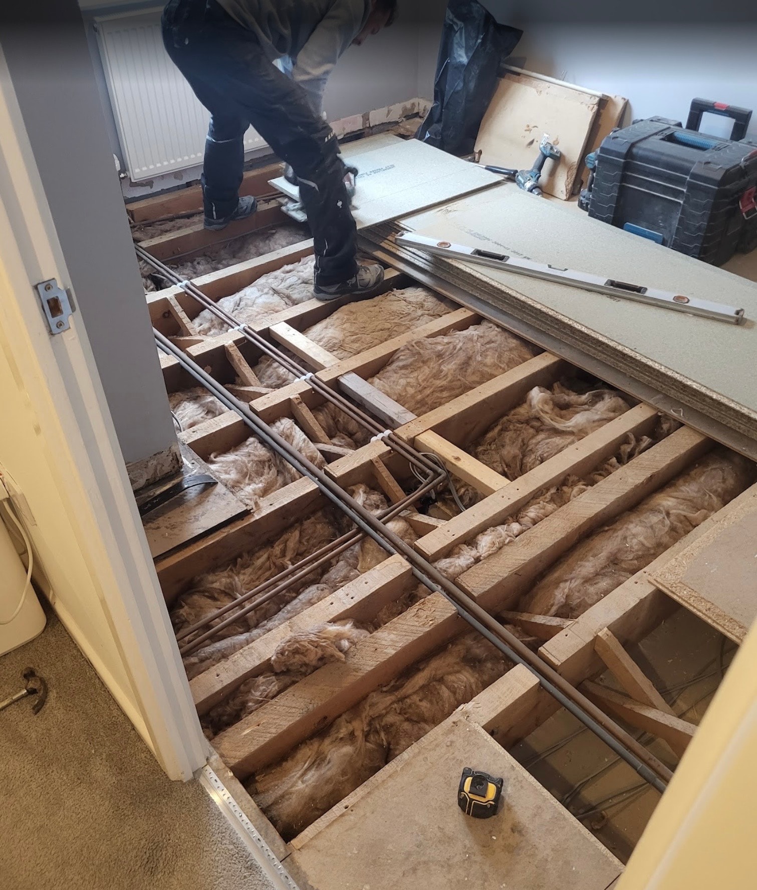 Floor renovation in progress, with the old boards lifted to expose the joists and insulation before the new floor is laid.