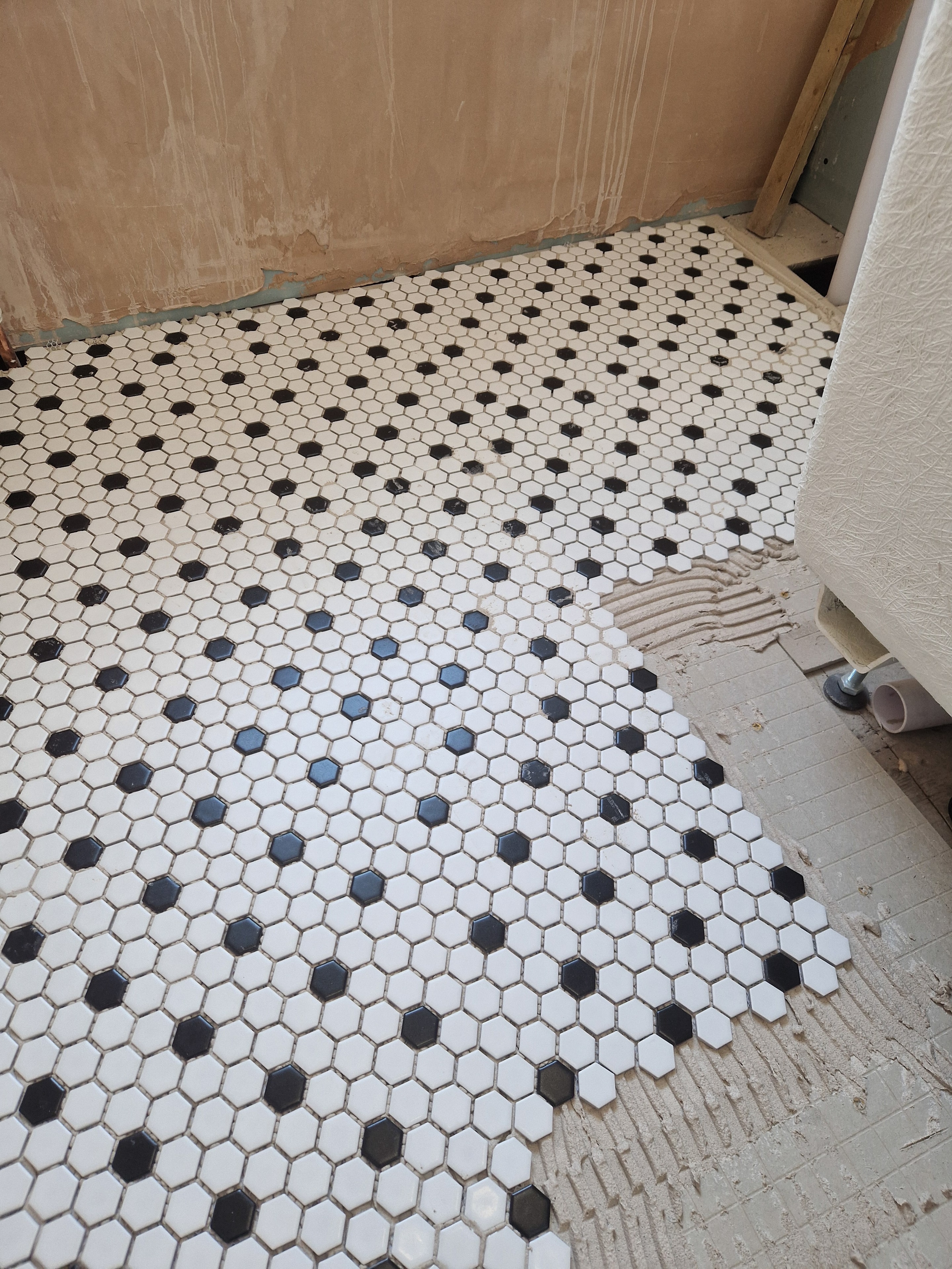 Black and white hexagonal floor tiling in progress, with the pattern carefully aligned across the room.